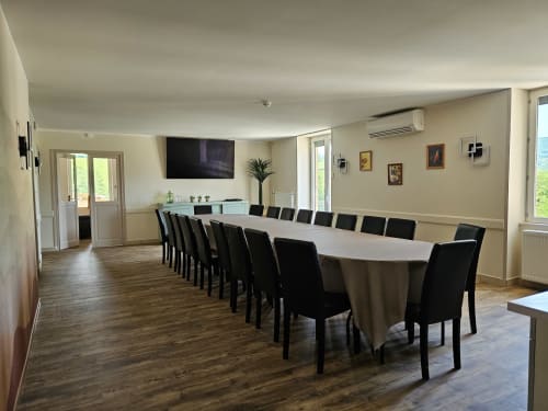 Salle à manger spacieuse aux Gîtes Les Muriers avec longue table, chaises noires, télévision et vue sur jardin à Bourgvilain