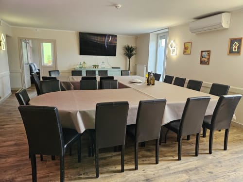 Spacieuse salle à manger des Gites Les Muriers avec table ovale, chaises noires, TV et équipements modernes à Bourgvilain.