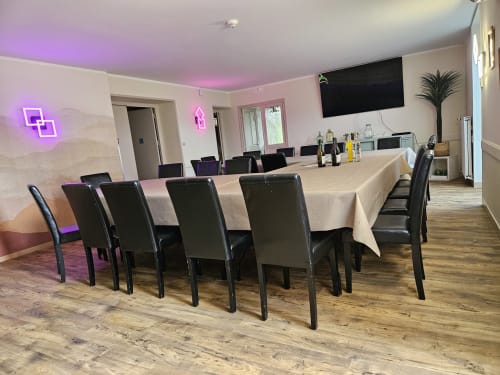 Salle à manger moderne aux Gîtes Les Muriers avec longue table, chaises noires, éclairage rose fluo et télévision pour groupes