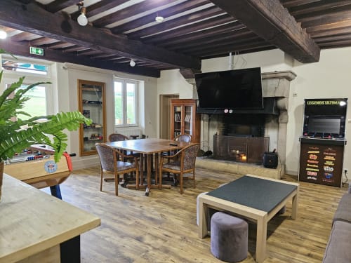 Spacieux séjour du gîte Les Muriers à Bourgvilain avec table à manger, cheminée, TV, borne d'arcade et vue sur le jardin