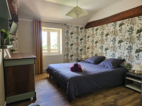 Chambre moderne aux Gites Les Muriers avec papier peint botanique, lit double, poutres en bois et portes-fenêtres à Bourgvilain