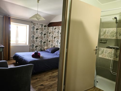 Chambre avec literie bleue et papier peint botanique aux Gîtes Les Muriers, Bourgvilain, douche attenante visible