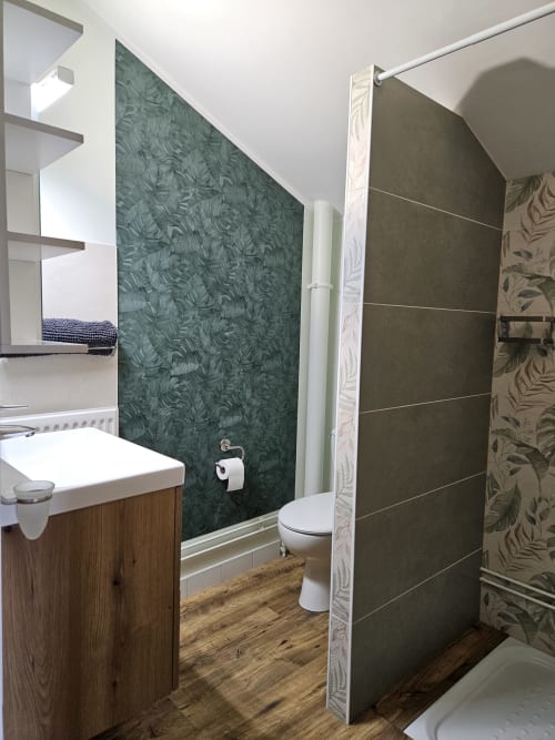 Salle de bain moderne au Gîte Ornella des Gîtes Les Muriers avec mur à motifs verts, meuble-lavabo en bois, toilettes et douche
