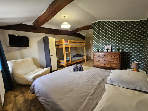 Chambre spacieuse au Gîte Ornella à Bourgvilain avec lit double, lits superposés, poutres en bois et papier peint à motifs verts