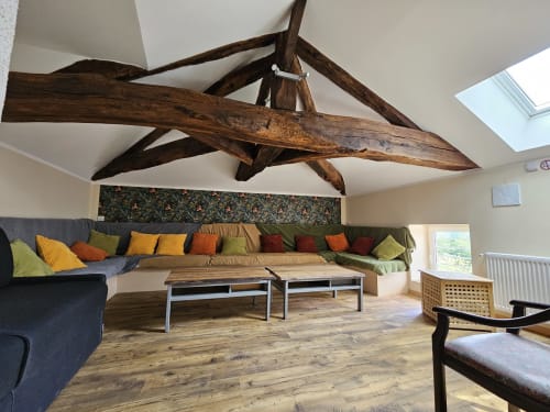 Spacieuse salle de séjour du Gîte Ornella avec poutres apparentes, sièges aux coussins colorés et tables basses en bois