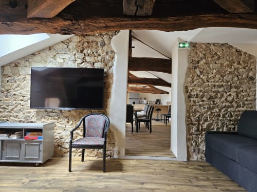 Intérieur rustique en pierre avec TV écran plat, poutres en bois et salon aménagé aux Gites Les Muriers, Bourgvilain