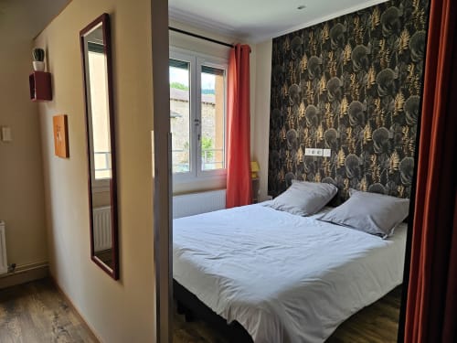 Chambre moderne aux Gites Les Muriers à Bourgvilain avec lit queen-size, papier peint orné et portes-fenêtres rouges