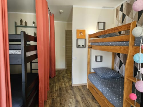 Chambre lumineuse aux Gîtes Les Muriers avec lits superposés en bois, rideaux corail, linge de lit à motifs et décoration colorée