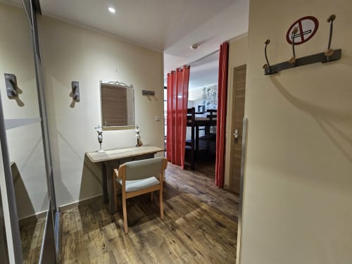 Chambre du Gîte Ornella avec coiffeuse, miroir, chaise en bois, rideaux rouges et parquet aux Gîtes Les Murriers