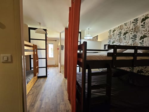 Chambre de dortoir spacieuse aux Gites Les Muriers avec lits superposés noirs, parquet, poutre rouge et papier peint floral