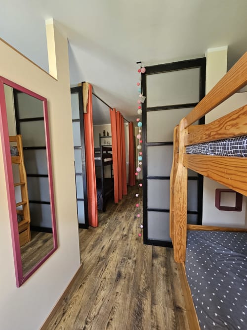 Chambre de dortoir aux Gites Les Muriers avec lits superposés en bois, séparations de rideaux colorés et parquet à Bourgvilain