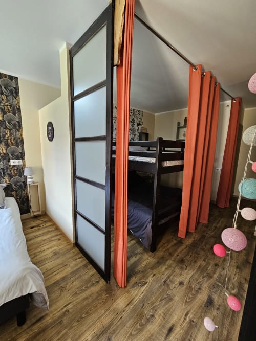 Chambre partagée aux Gîtes Les Muriers avec lits superposés noirs, rideaux de confidentialité rouges et sol en bois à Bourgvilain.