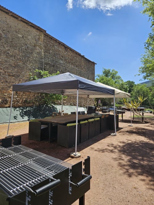 Espace de restauration extérieure avec auvents blancs, tables de repas sombres et grils intégrés aux Gites Les Muriers à Bourgvilain