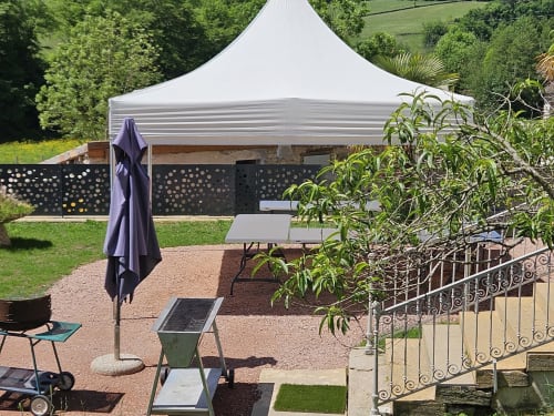 Vue du jardin du Gîte Le Tilleul aux Gîtes Les Muriers avec terrasse élégante, tente blanche, parasol et verdure luxuriante