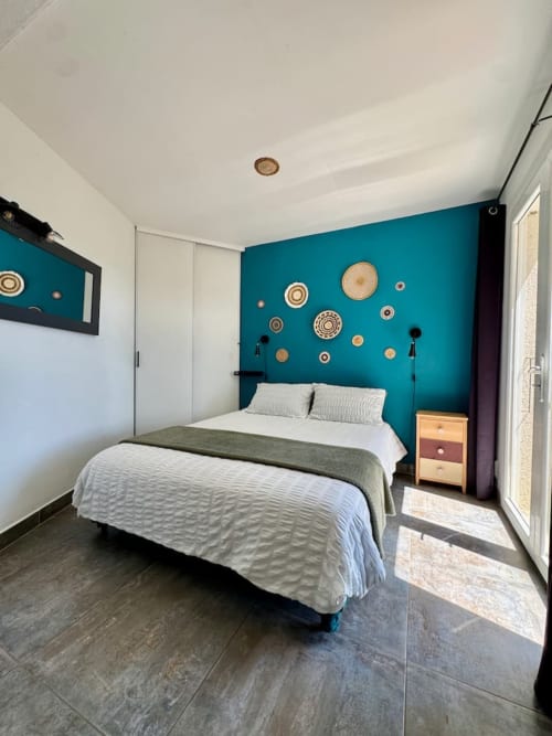 Chambre de villa moderne avec mur d'accent teal, literie blanche, décoration murale en osier et parquet foncé aux Villas