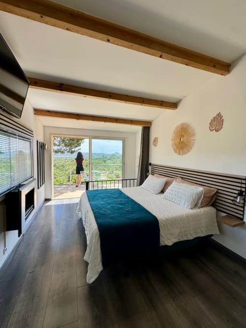 Chambre moderne de la Villa Anchorage avec balcon vue mer, poutres en bois, lit queen-size, TV et paysage méditerranéen