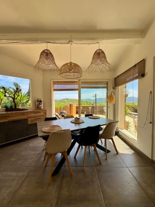 Salle à manger contemporaine dans une villa de Porto-Vecchio avec vue sur la mer, luminaires suspendus en fibres tressées et mobilier design