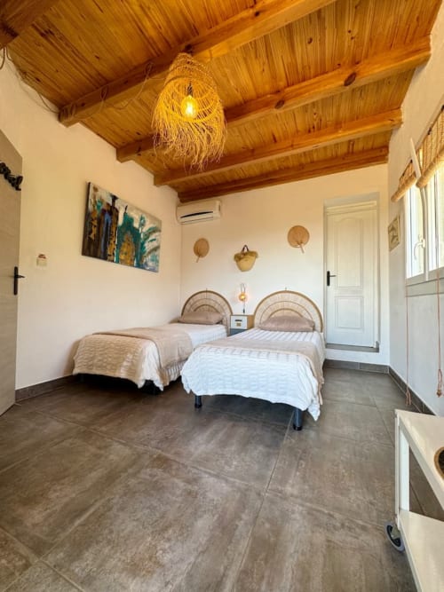 Lits jumeaux aux têtes de lit tressées dans une chambre lumineuse avec poutres apparentes et carrelage en terre cuite à Les