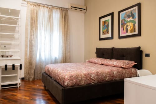 Camera Vittoria presso ROOMITO APARTMENTS Napoli, con letto nero con biancheria rosa, pavimenti in legno e pareti gialle