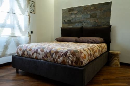 Camera da letto moderna con letto in legno scuro, copriletto fantasia e parete in pietra - ROOMITO APARTMENTS, Napoli