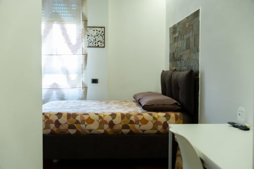Camera moderna di ROOMITO APARTMENTS Napoli con biancheria decorata, testata scura, scrivania e finestra con vista città e persiane