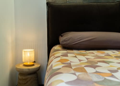 Accogliente camera da letto ROOMITO a Napoli con lampada da comodino illuminata, biancheria a motivi e testata scura