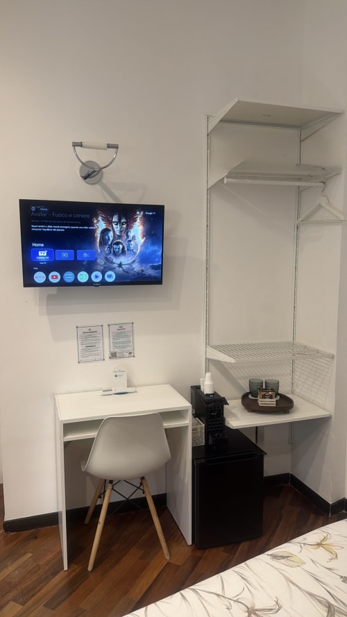 Moderna zona di lavoro in camera d'hotel presso Roomito Apartments Napoli con scrivania, sedia, TV a muro che mostra Avatar, mobile con ripiani e