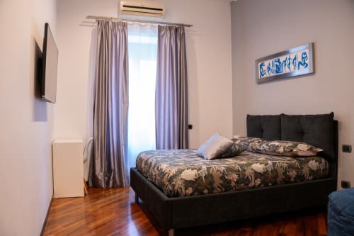 Camera Leonardo bedroom at ROOMITO APARTMENTS Naples with black bed, patterned bedding, purple curtains, TV, and wooden