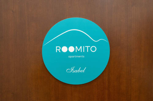 Logo circolare turchese di ROOMITO Apartments Isabel su fondo in legno, Napoli