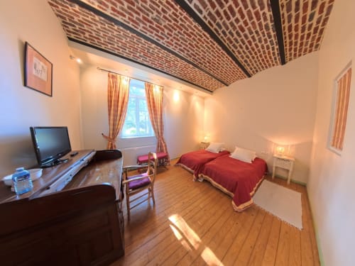 Ferme De La Sensee red bedroom with wooden floor, TV desk, bed with red bedding, and exposed brick ceiling
