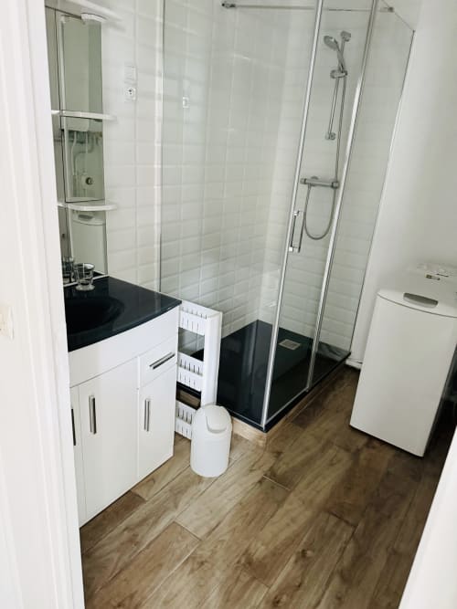 Salle de bain moderne du gîte Maison Nolette avec vasque blanche, plan de travail noir, douche à l'italienne et parquet