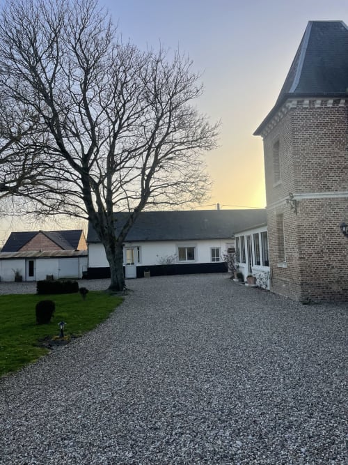 Cottage Maison Nolette à la Baie de Somme : cour gravillonnée, arbre dénudé, clocher en brique, bâtiments blancs au crépuscule