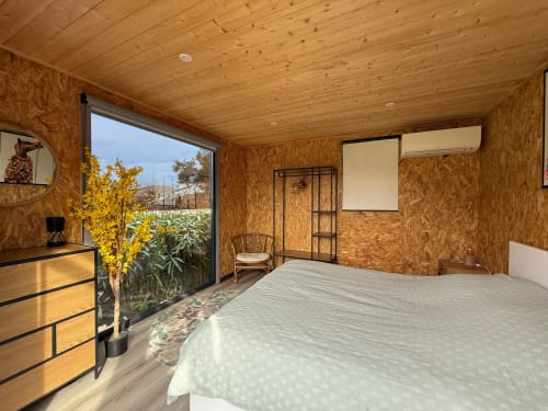 Camera da letto moderna con pareti in sughero e soffitto in legno nella villa di Porticcio, vista sul giardino con piante e fiori