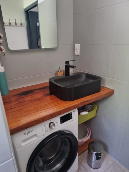 Bagno compatto con lavabo nero su piano in legno, lavatrice sottostante, piastrelle, specchio e rubinetto moderno