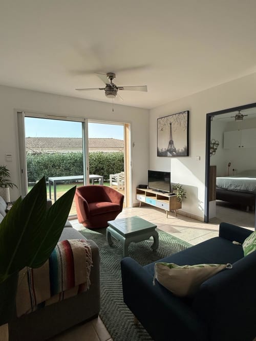 Luminosa sala in villa Porticcio con poltrona rossa, vista giardino, ventilatore e arredi moderni