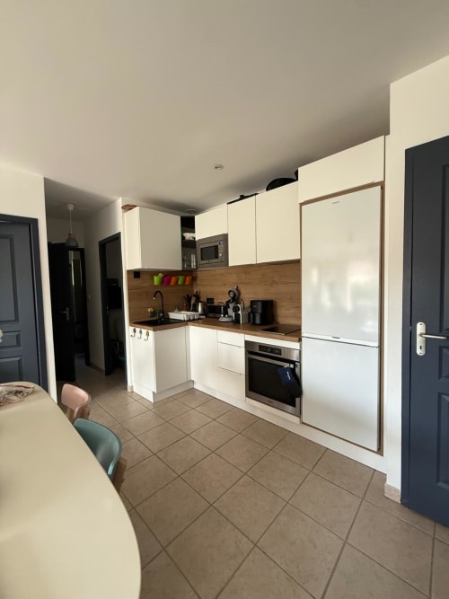 Cucina moderna con mobili bianchi, rivestimento in legno e elettrodomestici in acciaio inox a Villa Conciergerie De Porticcio