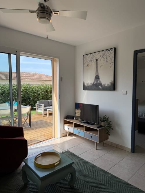 Soggiorno moderno con TV, porte-finestre verso il giardino, opera raffigurante la Torre Eiffel, ventilatore a soffitto alla Conciergerie De Porticcio