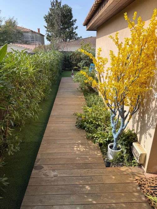 Sentiero in legno tra i giardini fioriti di Villa Conciergerie De Porticcio, con alberi in fiore e siepi