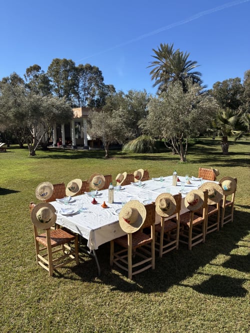 Grande table de salle à manger en plein air avec chapeaux de paille à Villa Elo, Marrakech, entourée d'oliviers