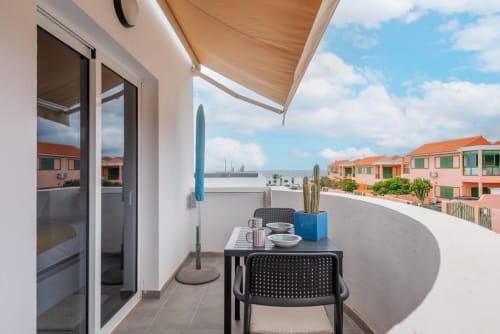 Soleado balcón del apartamento Casa Sol con vista al mar, mesa de comedor, cactus y vista del pueblo costero de Tarajalejo