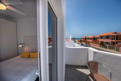Dormitorio del apartamento Casa Sol con balcón con vista al mar sobre Tarajalejo, Fuerteventura. Paredes blancas, almohadas amarillas, costero