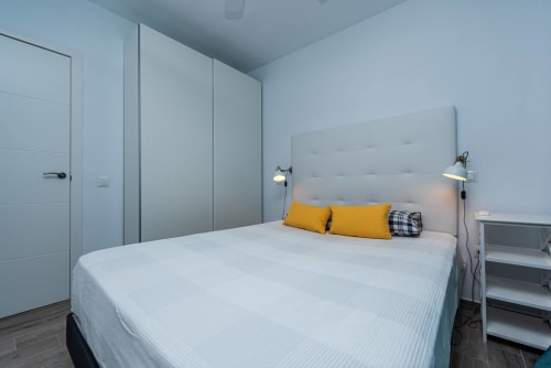 Moderno dormitorio en Smart Rent Fuerteventura en Tarajalejo con cama matrimonial, almohadas amarillas, paredes azul claro y armario empotrado