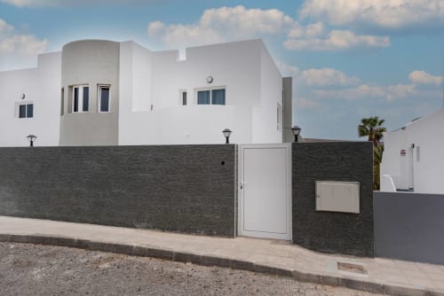 Moderno edificio blanco con muro de piedra oscura y puerta en Tarajalejo, Fuerteventura, propiedad Casa Sol