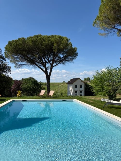 Piscine étincelante bleu turquoise au Domaine les Olivoux avec pin parasol, transats et chaumière à Pomport