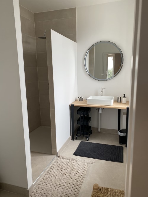 Salle de bain moderne au gîte Le Domaine les Olivoux à Pomport avec miroir rond, vasque blanche et douche à l'italienne