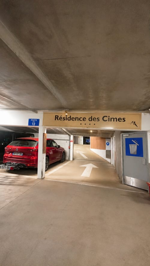 Entrée du parking souterrain du Chalet des Cimes avec voitures rouges et panneau Résidence des Cimes