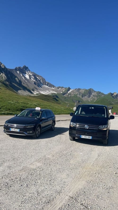 Véhicules de taxi et navette garés au Chalet des Cimes à Belle Plagne, avec les montagnes alpines et prairies verdoyantes en arrière-plan