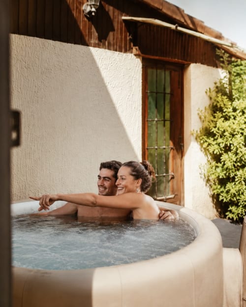 Couple relaxing in private hot tub at Les Chalets de Mosnay cottage with garden view, Mosnay