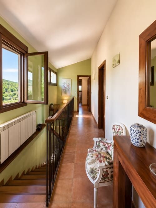 Pasillo luminoso en villa de Baiona con paredes verde lima, puertas de madera, suelo de terracota y vistas a la montaña desde las ventanas