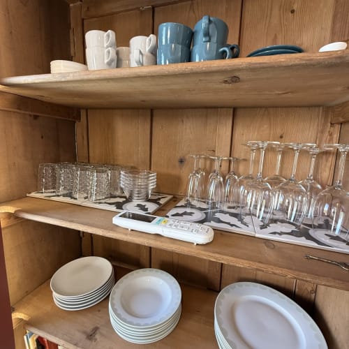Étagères de meuble en bois à la villa Maisons Le Clos Du Moulin exposant des tasses blanches, des cruches bleues, de la verrerie et des articles empilés